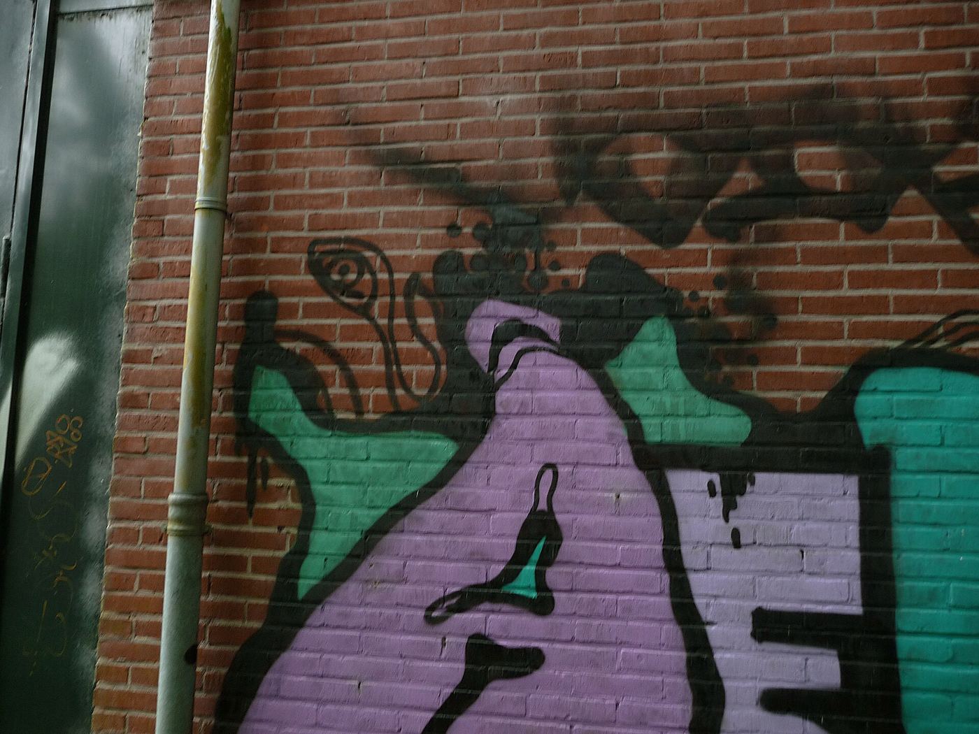 Purple and teal graffiti lettering painted on a brick wall