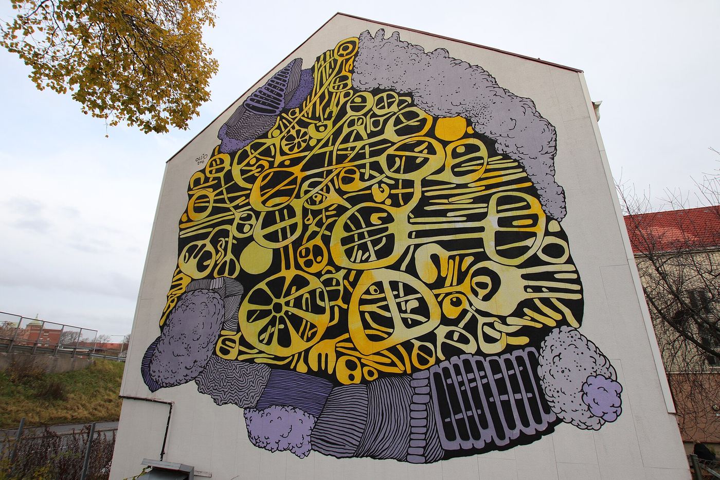 Yellow and violet organic-pattern mural on a building gable under autumn trees