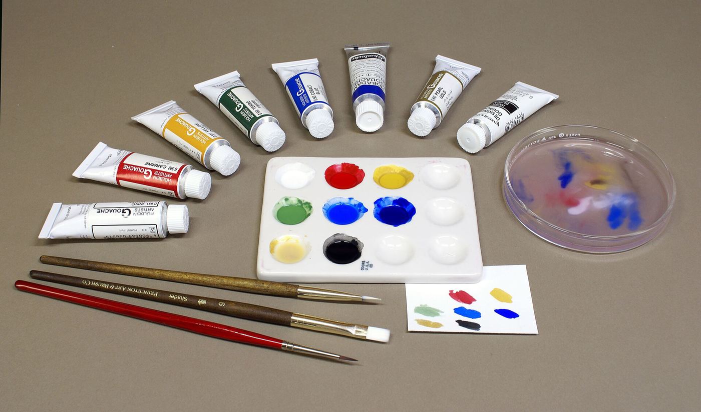 Tubes of gouache fanned around a palette with brushes