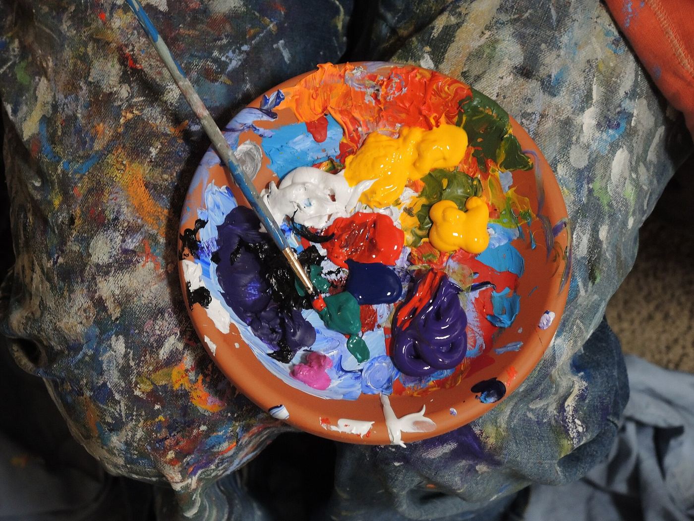 Clay bowl full of mixed bright paints with a brush