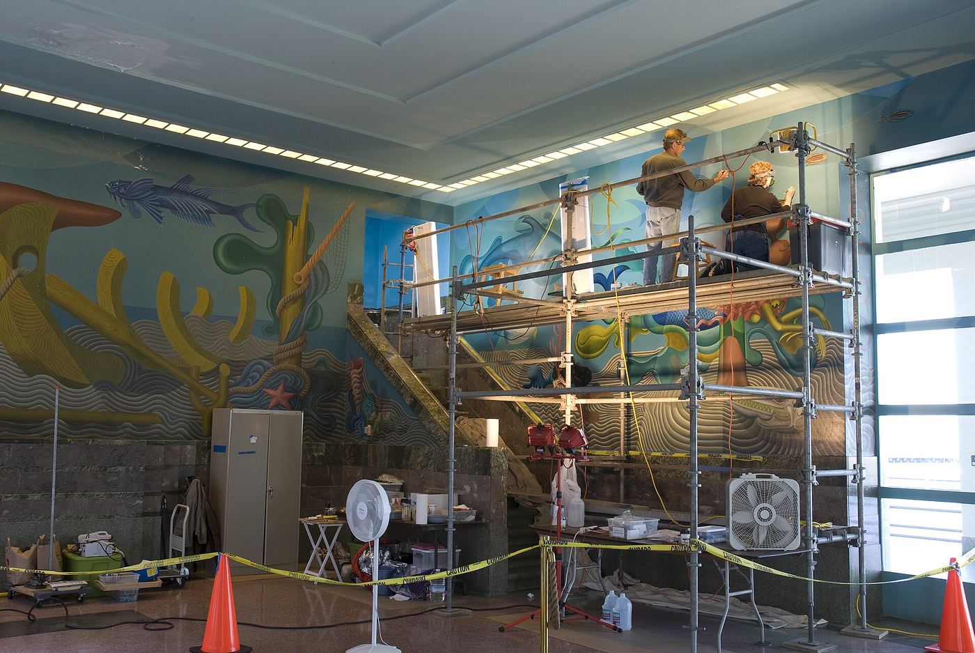 Restoration team on scaffolding in front of a large colourful public mural