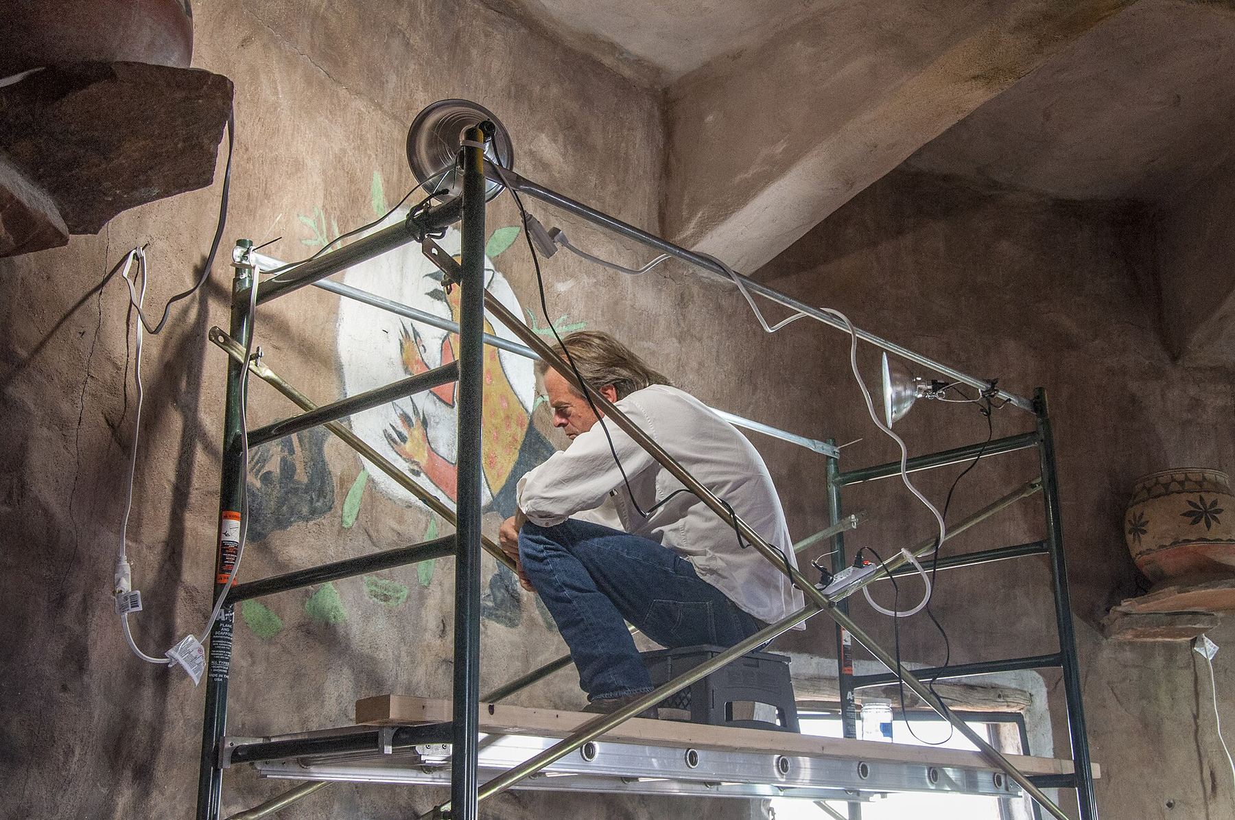Conservator on scaffolding restoring a painted wall mural indoors