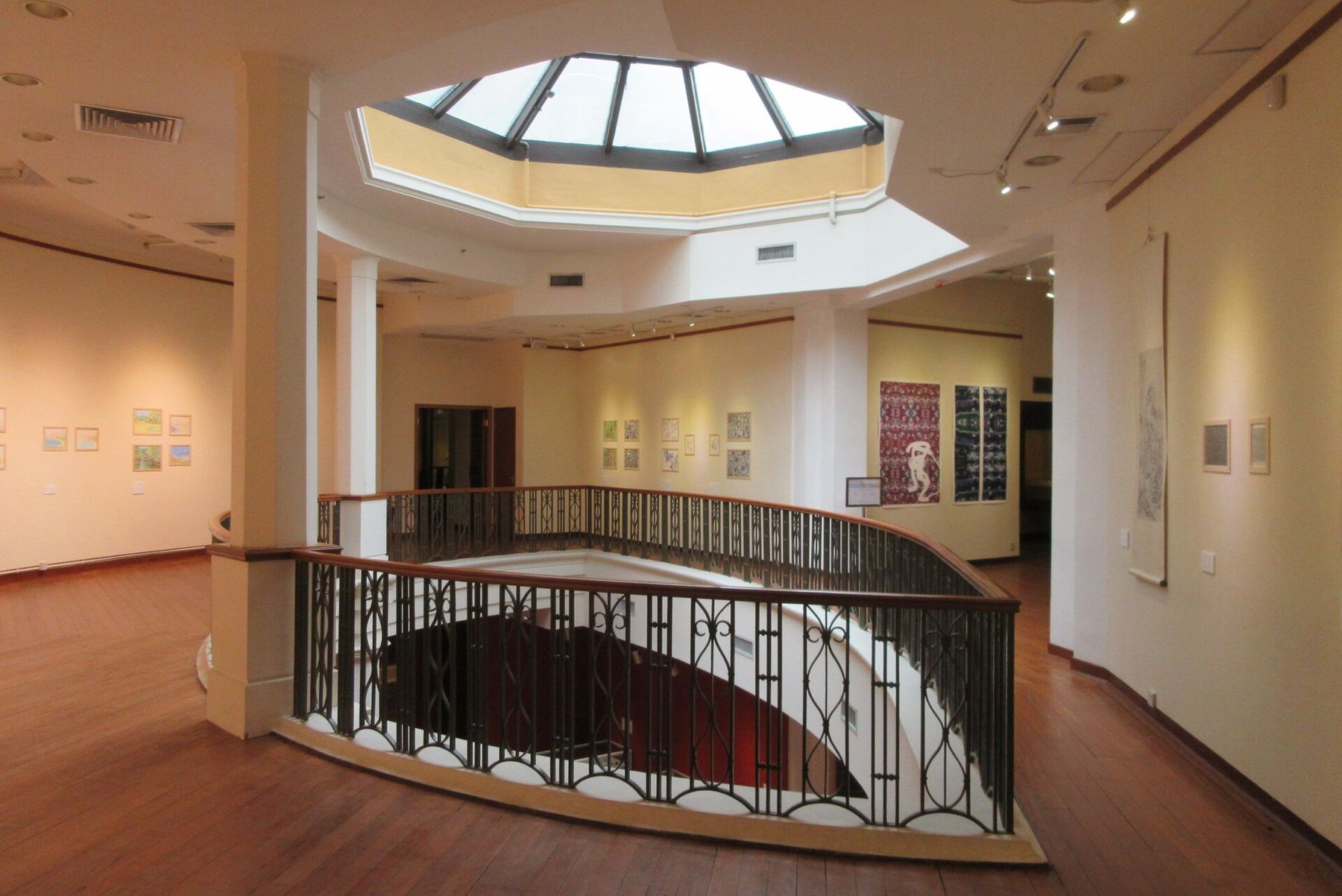 Two-level gallery hall with a skylight, wooden floors and framed works on white walls