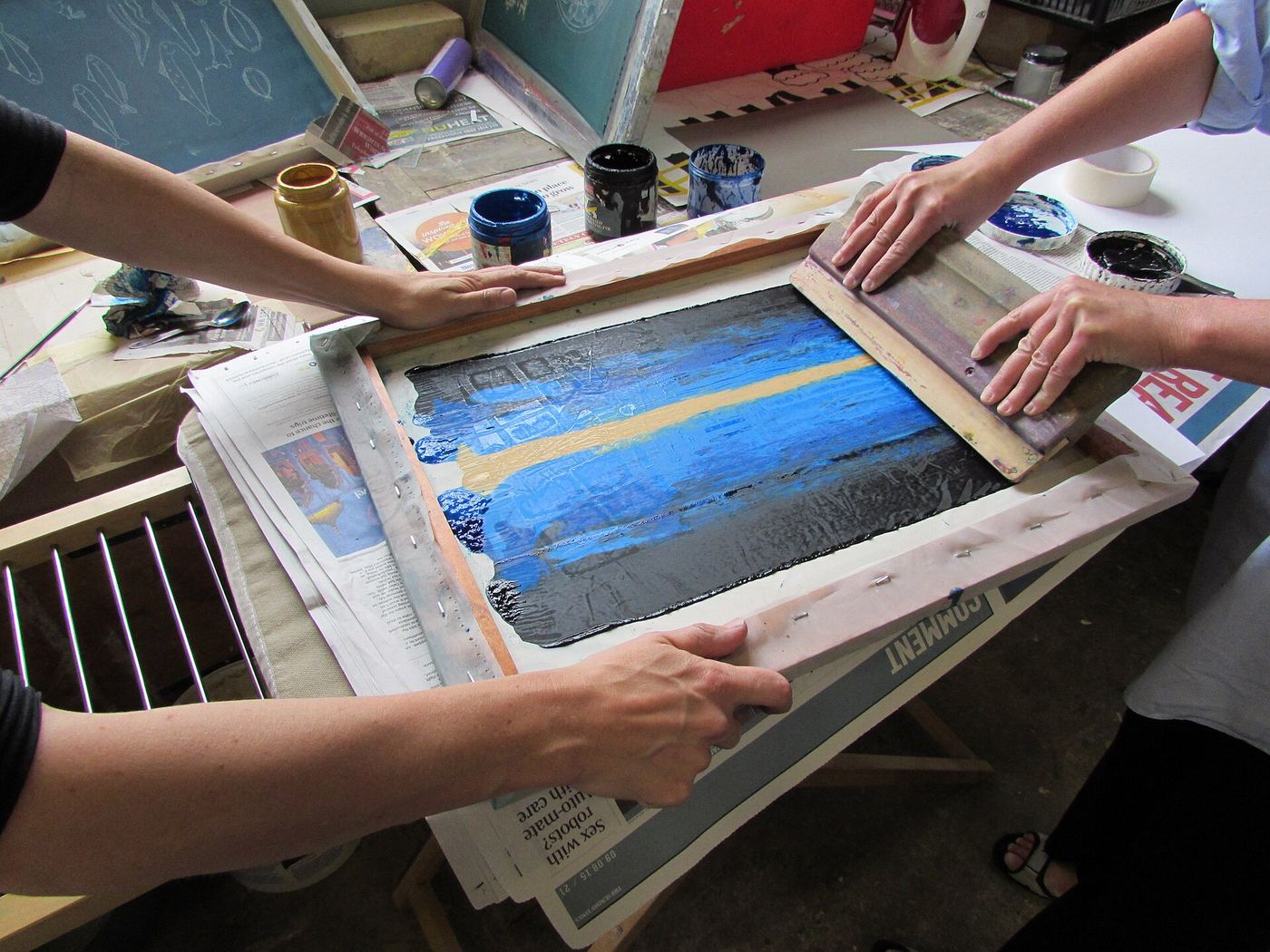 Two people pulling ink across a blue screen print