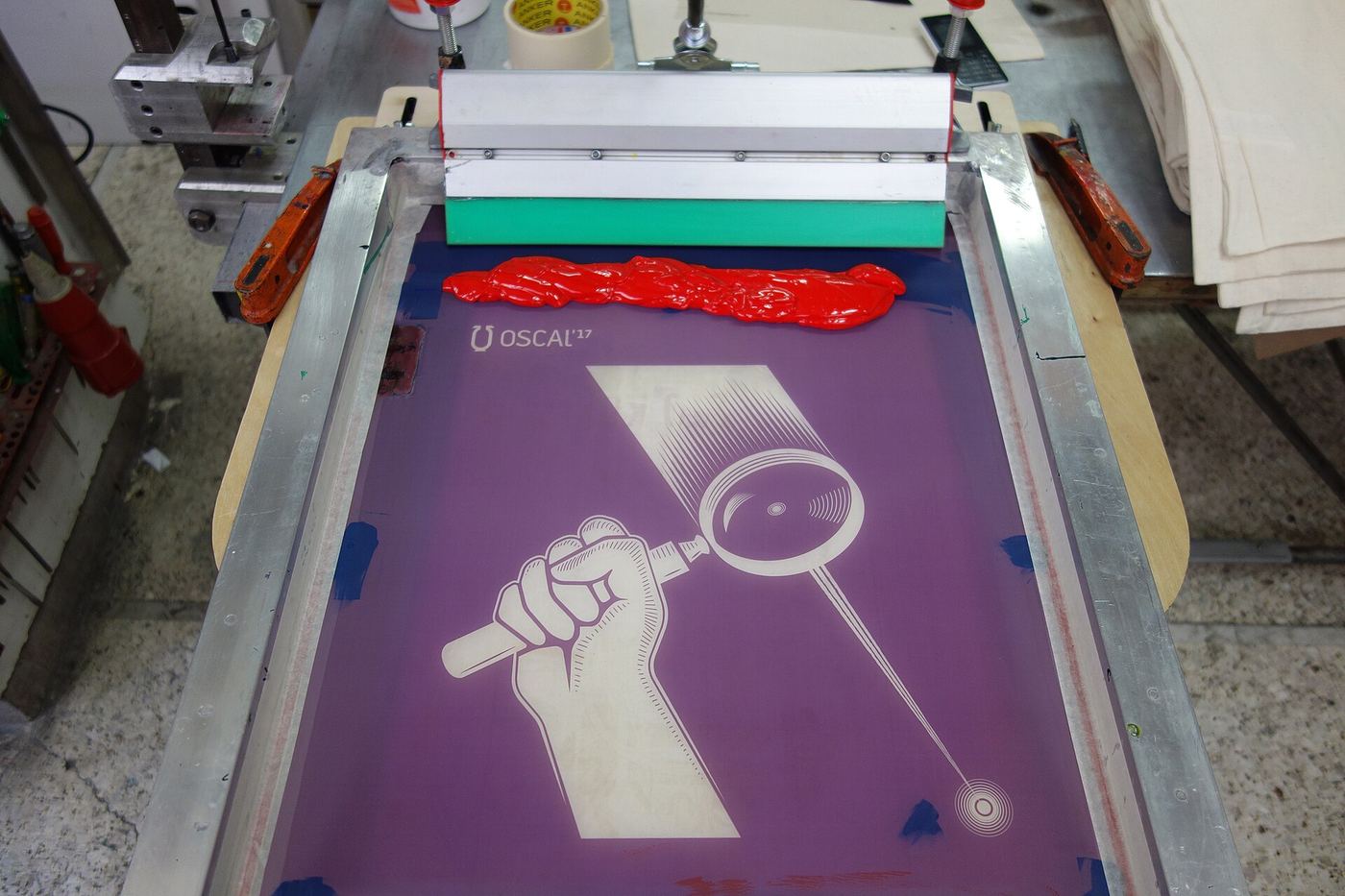 Purple silkscreen with a raised-fist illustration on a press, red ink on the squeegee