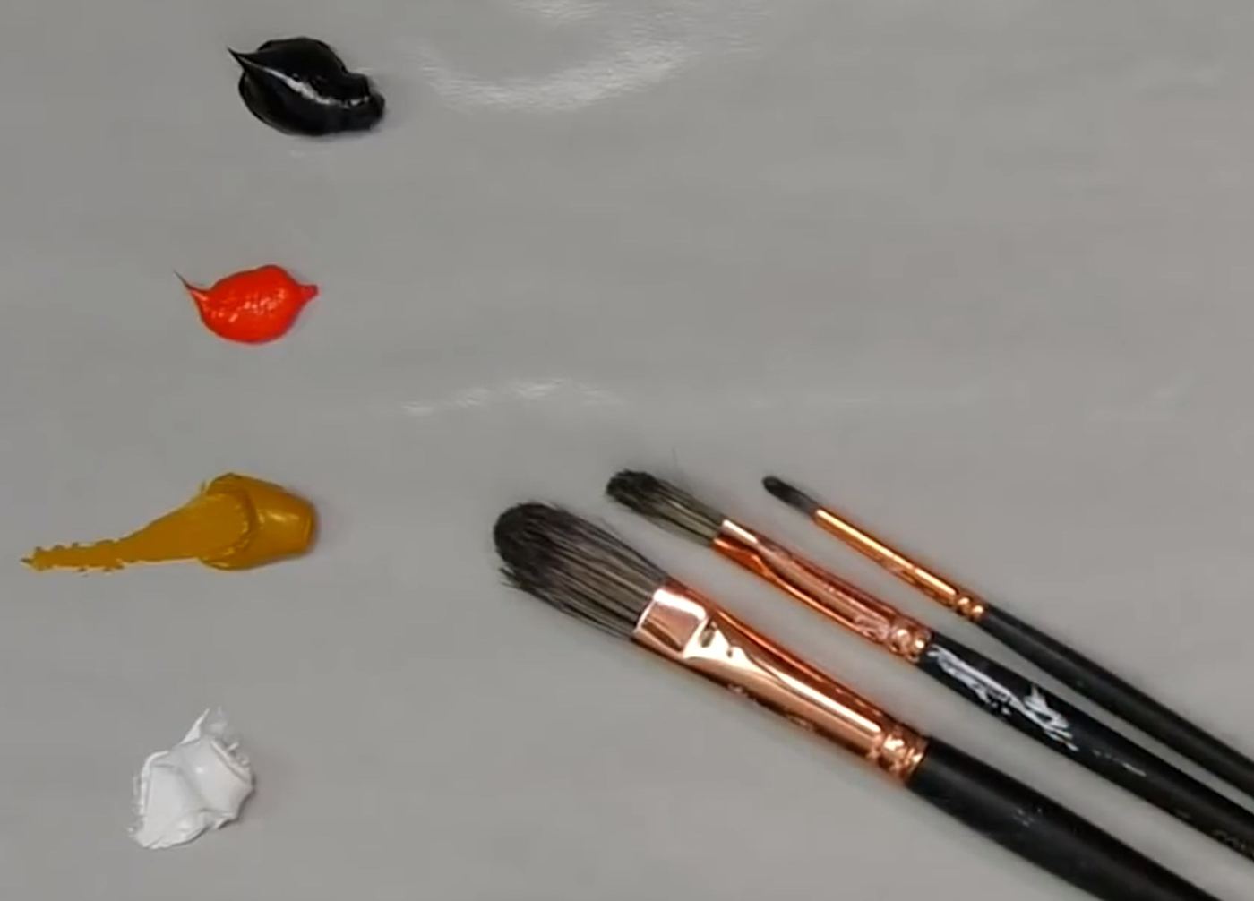 Dabs of black, red, ochre and white paint beside three brushes